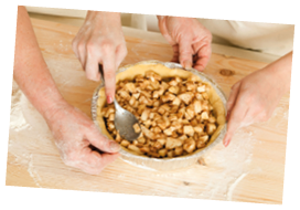 hands of the grandmother and hand of the granddaughter stack a stuffing in a form for pie